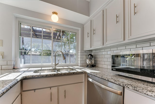 kitchen with sink, dishwasher, white cabinets, light stone countertops, and backsplash