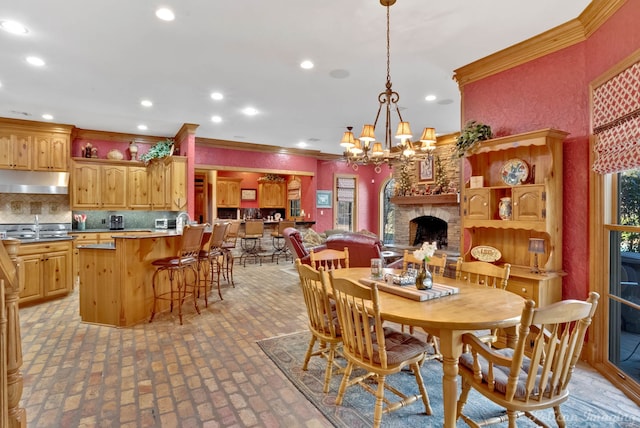 dining room with sink, a stone fireplace, crown molding, and a chandelier