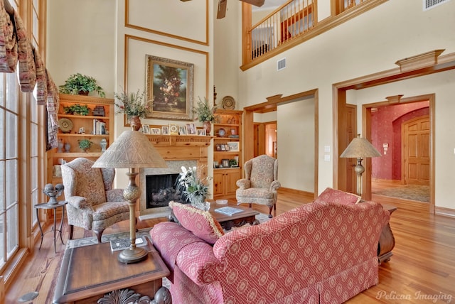 living room featuring a towering ceiling, a premium fireplace, ceiling fan, and light hardwood / wood-style flooring