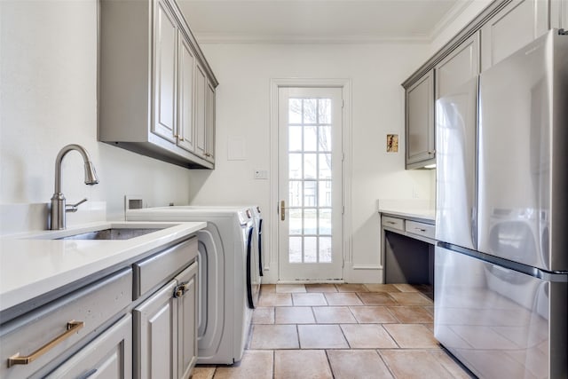 clothes washing area with washing machine and dryer, sink, ornamental molding, light tile patterned floors, and cabinets