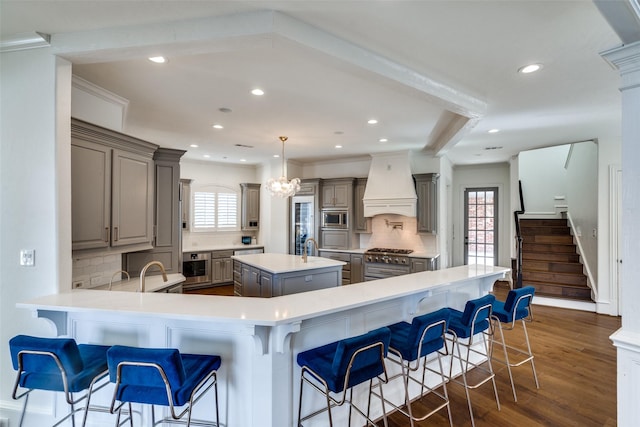 kitchen featuring a kitchen island, custom exhaust hood, kitchen peninsula, appliances with stainless steel finishes, and a kitchen breakfast bar