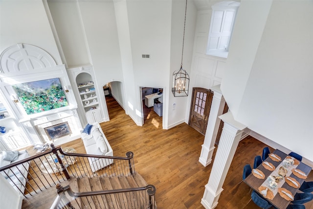 staircase with a high ceiling, built in features, an inviting chandelier, and hardwood / wood-style floors