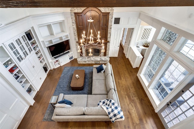 living room featuring built in shelves, dark hardwood / wood-style floors, a towering ceiling, and a chandelier