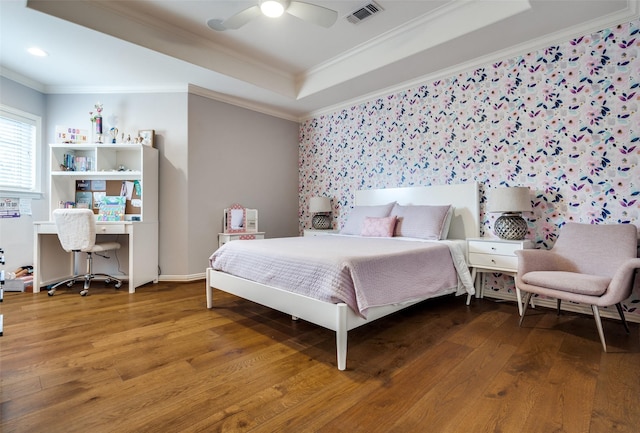 bedroom with ceiling fan, a tray ceiling, ornamental molding, and hardwood / wood-style floors