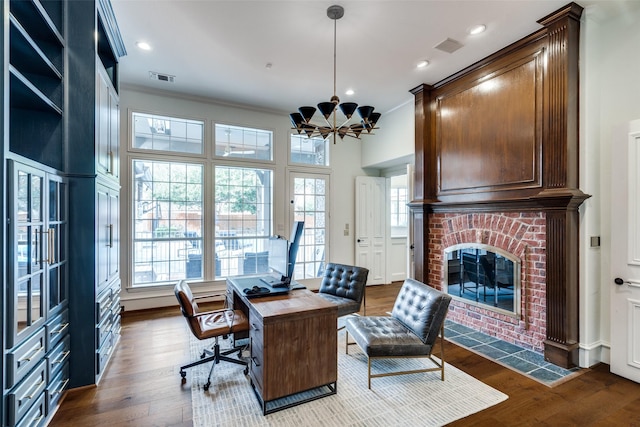 office area featuring a brick fireplace, dark wood-type flooring, ornamental molding, and an inviting chandelier