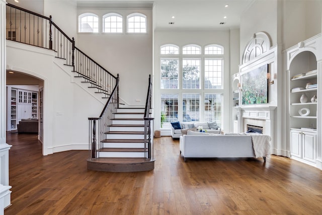 unfurnished living room with a high ceiling, dark hardwood / wood-style floors, built in features, and ornamental molding