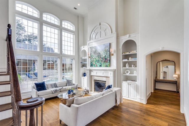 living room with a fireplace, built in features, a high ceiling, and dark wood-type flooring