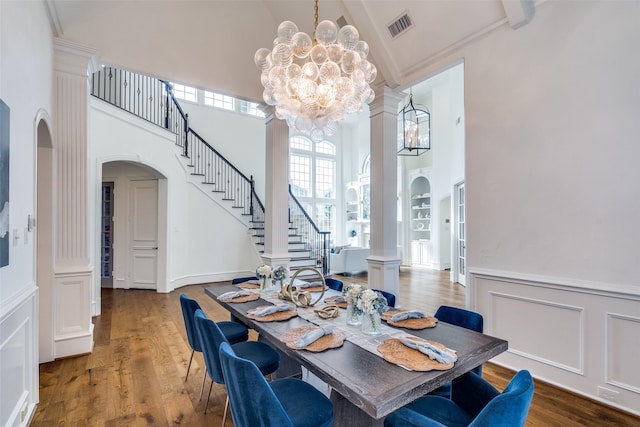 dining space with wood-type flooring, an inviting chandelier, a high ceiling, ornamental molding, and ornate columns