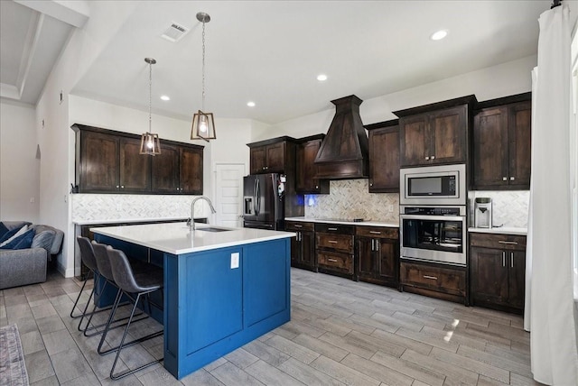 kitchen with sink, custom range hood, pendant lighting, dark brown cabinetry, and black appliances