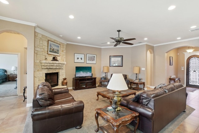 living room with ceiling fan, light tile patterned floors, crown molding, and a stone fireplace