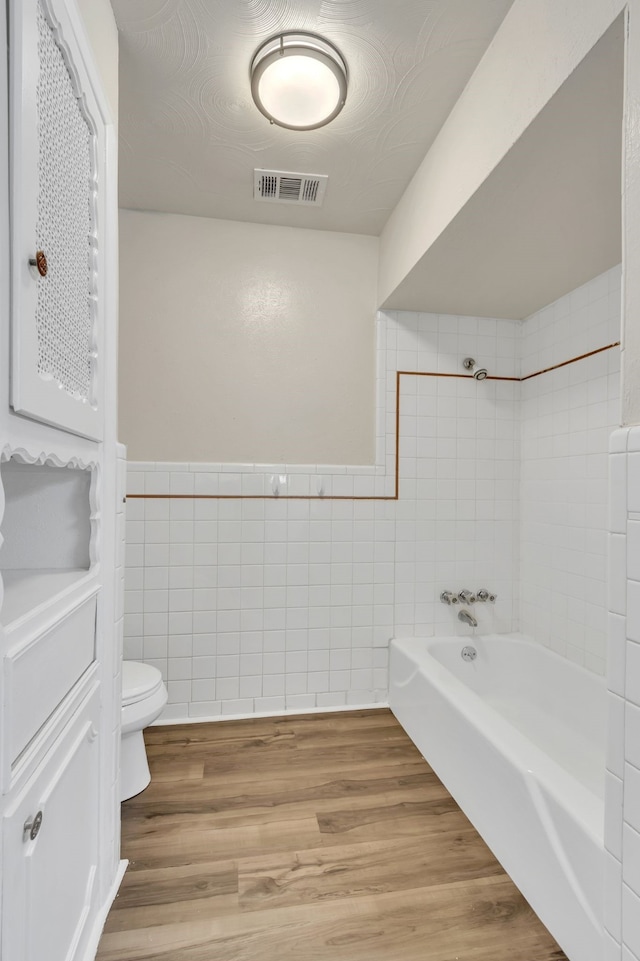 bathroom featuring toilet, tile walls, hardwood / wood-style floors, and tiled shower / bath