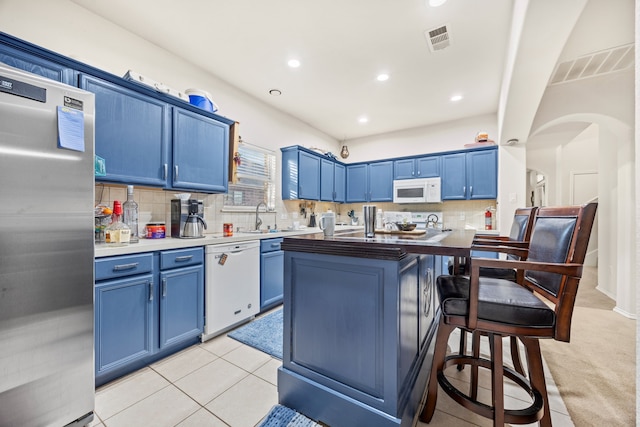 kitchen featuring white appliances, a breakfast bar area, light tile patterned floors, decorative backsplash, and blue cabinets