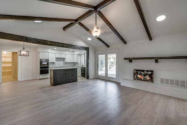 unfurnished living room with sink, a fireplace, light wood-type flooring, and vaulted ceiling with beams