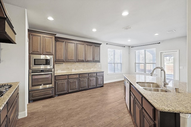 kitchen with premium range hood, light hardwood / wood-style flooring, stainless steel appliances, an island with sink, and sink