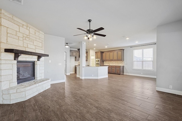 unfurnished living room with dark wood-type flooring, ceiling fan, and a stone fireplace