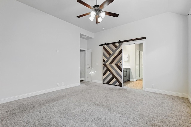 empty room with ceiling fan, light colored carpet, vaulted ceiling, and a barn door