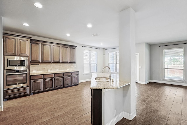 kitchen featuring light stone counters, sink, backsplash, appliances with stainless steel finishes, and dark brown cabinetry