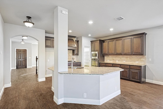 kitchen with stainless steel appliances, sink, wood-type flooring, decorative backsplash, and light stone countertops