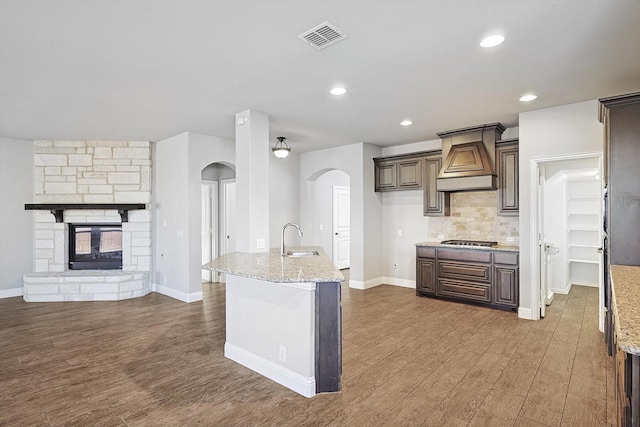 kitchen featuring light stone countertops, premium range hood, sink, stainless steel gas cooktop, and a stone fireplace