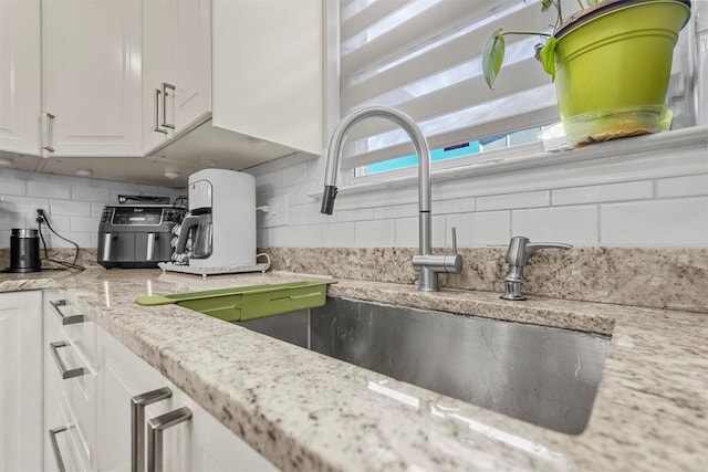 kitchen featuring white cabinets, light stone countertops, and decorative backsplash