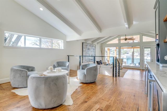 living area with ceiling fan, a wealth of natural light, vaulted ceiling with beams, and light hardwood / wood-style floors