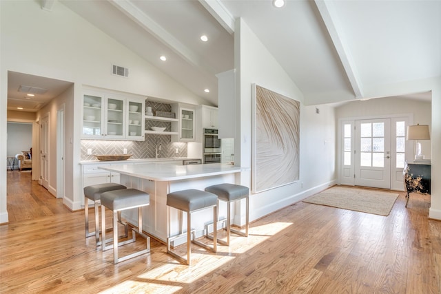 kitchen featuring kitchen peninsula, tasteful backsplash, beam ceiling, a breakfast bar area, and white cabinetry