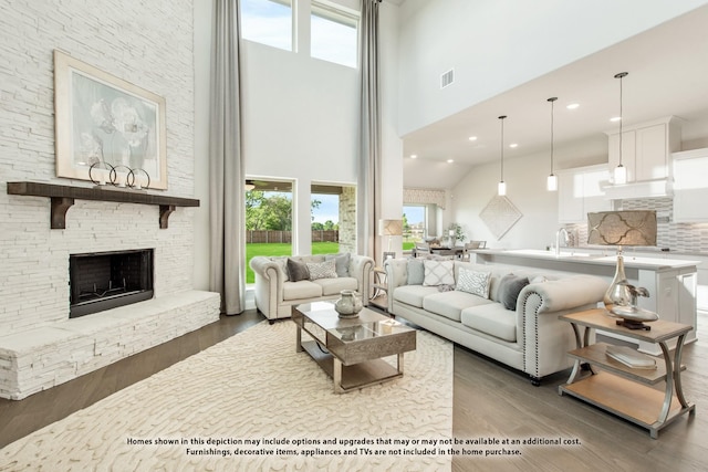 living room featuring a high ceiling, a stone fireplace, sink, and dark hardwood / wood-style floors