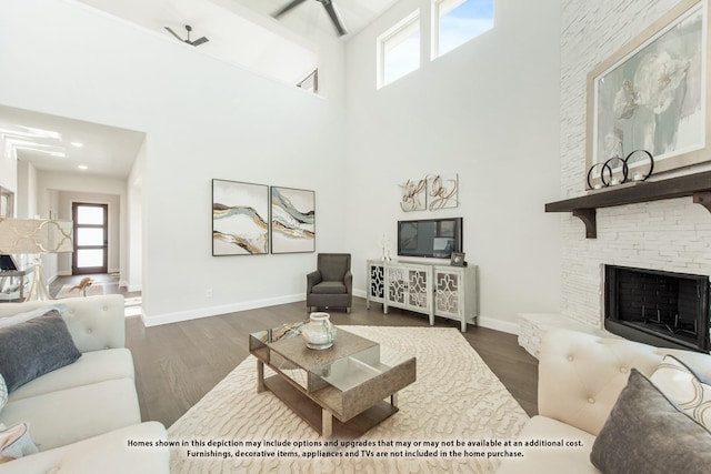 living room featuring dark hardwood / wood-style floors, a high ceiling, ceiling fan, and a stone fireplace