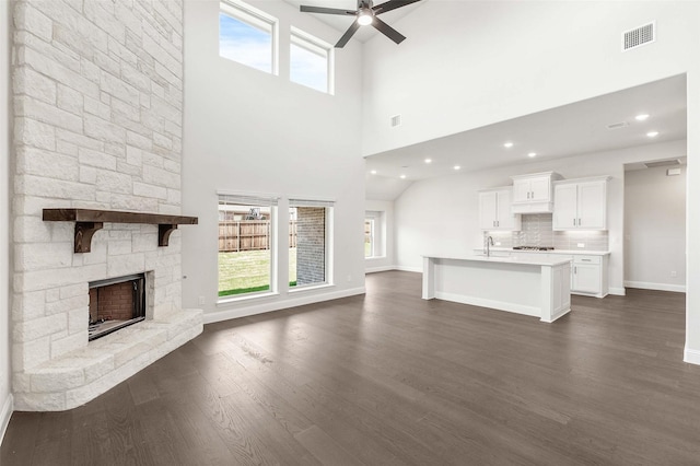 unfurnished living room with ceiling fan, dark wood-type flooring, visible vents, and a fireplace