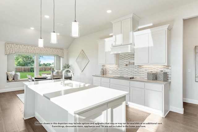 kitchen with a kitchen island with sink, vaulted ceiling, hanging light fixtures, white cabinetry, and tasteful backsplash