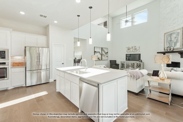 kitchen with stainless steel appliances, sink, white cabinets, light wood-type flooring, and a center island with sink