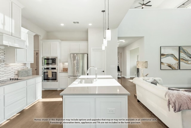 kitchen with a kitchen island with sink, hanging light fixtures, stainless steel fridge, white cabinets, and tasteful backsplash