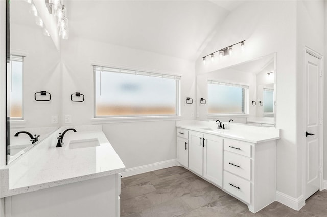 bathroom with vaulted ceiling, a sink, marble finish floor, baseboards, and two vanities
