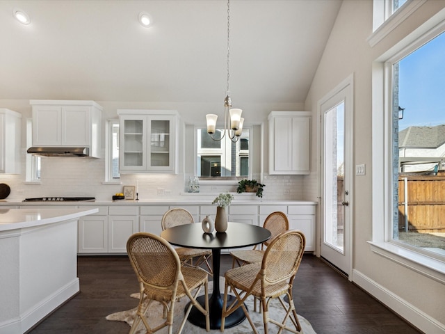 dining room with an inviting chandelier, a wealth of natural light, vaulted ceiling, and dark hardwood / wood-style floors