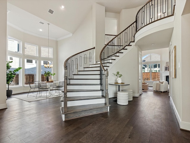 stairway featuring a towering ceiling, crown molding, a chandelier, and hardwood / wood-style floors