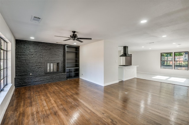 unfurnished living room featuring hardwood / wood-style floors, ceiling fan, a stone fireplace, and built in features