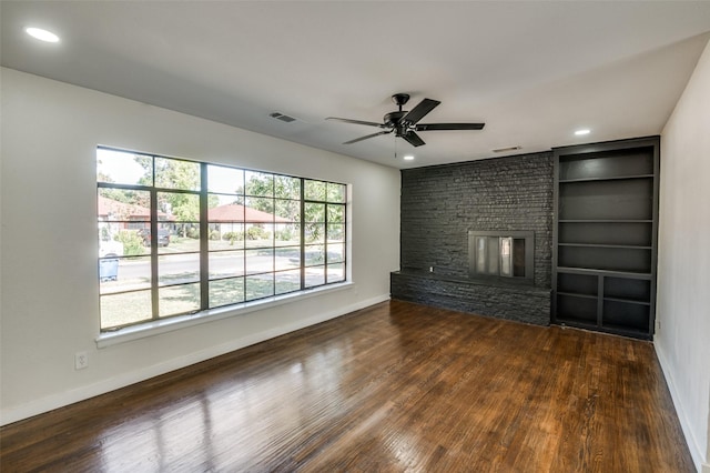 unfurnished living room featuring a large fireplace, ceiling fan, dark hardwood / wood-style floors, and built in shelves