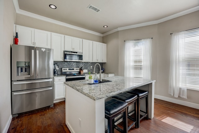 kitchen with dark wood-type flooring, light stone countertops, an island with sink, white cabinets, and appliances with stainless steel finishes