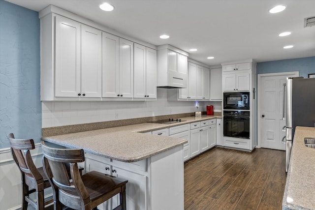 kitchen featuring white cabinets, a kitchen bar, black appliances, and kitchen peninsula