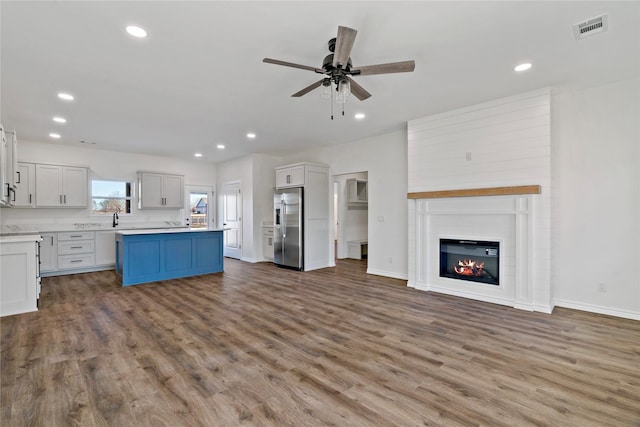 kitchen with light hardwood / wood-style floors, stainless steel fridge with ice dispenser, a center island, ceiling fan, and a fireplace