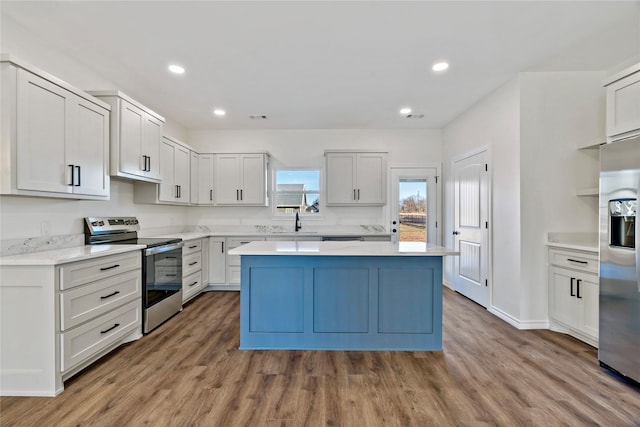 kitchen featuring wood-type flooring, appliances with stainless steel finishes, a kitchen island, white cabinets, and sink