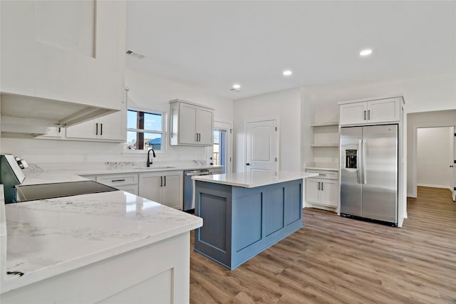 kitchen with a center island, light hardwood / wood-style floors, white cabinetry, appliances with stainless steel finishes, and sink