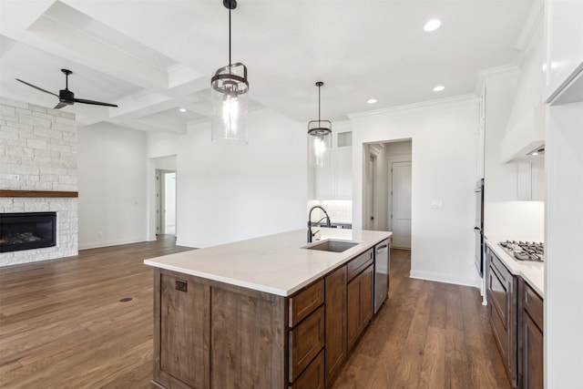 kitchen featuring dark wood-type flooring, a kitchen island with sink, stainless steel appliances, a stone fireplace, and a sink