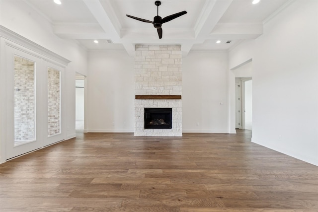 unfurnished living room with coffered ceiling, a ceiling fan, wood finished floors, beamed ceiling, and a stone fireplace