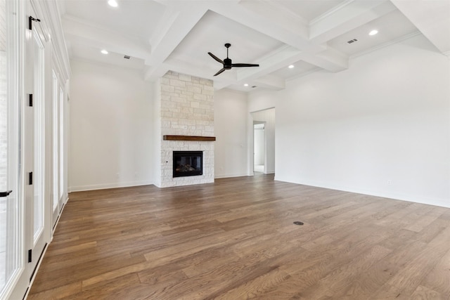 unfurnished living room with beam ceiling, ceiling fan, a stone fireplace, wood finished floors, and coffered ceiling