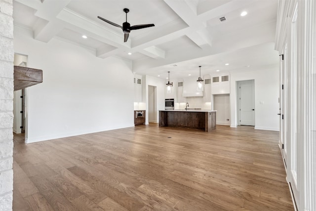 unfurnished living room with light wood-type flooring, beam ceiling, coffered ceiling, and a ceiling fan