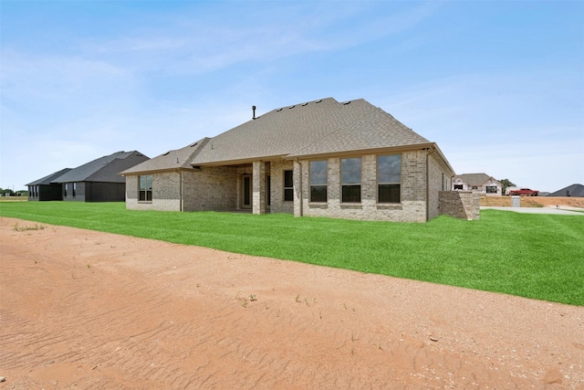 rear view of house featuring a shingled roof, brick siding, and a lawn