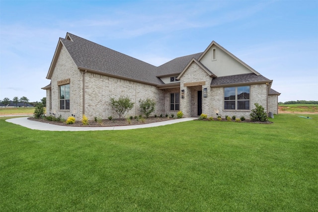 french country home with brick siding, a shingled roof, and a front yard