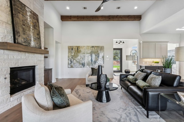 living room featuring light wood-type flooring, beam ceiling, and a stone fireplace