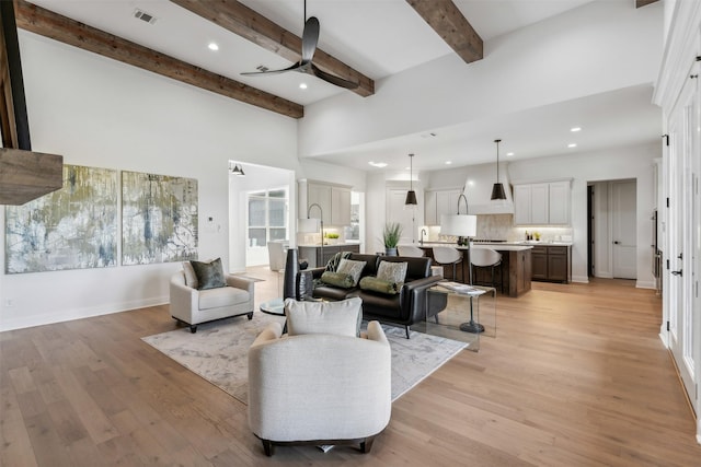 living room with light wood-type flooring, ceiling fan, and beamed ceiling